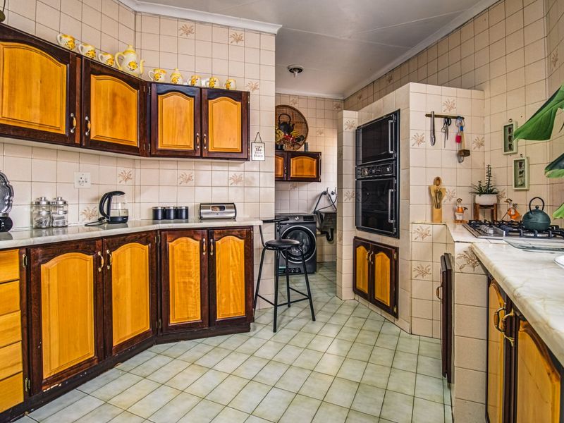 A functional kitchen featuring traditional wooden cabinetry, tiled splashbacks, built-in oven, and gas hob, with an adjacent laundry area.