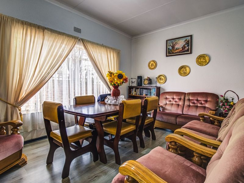 A dining room featuring light-toned laminate flooring and large windows with curtain rails, providing a functional space for family meals.