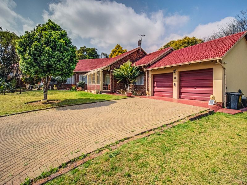 Front view of a single-story brick house featuring a paved driveway, double garage, and well-maintained garden area.