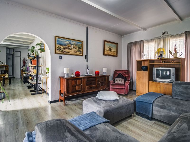 A living room featuring laminate flooring, exposed ceiling beams, and an arched entryway leading to an adjacent space.