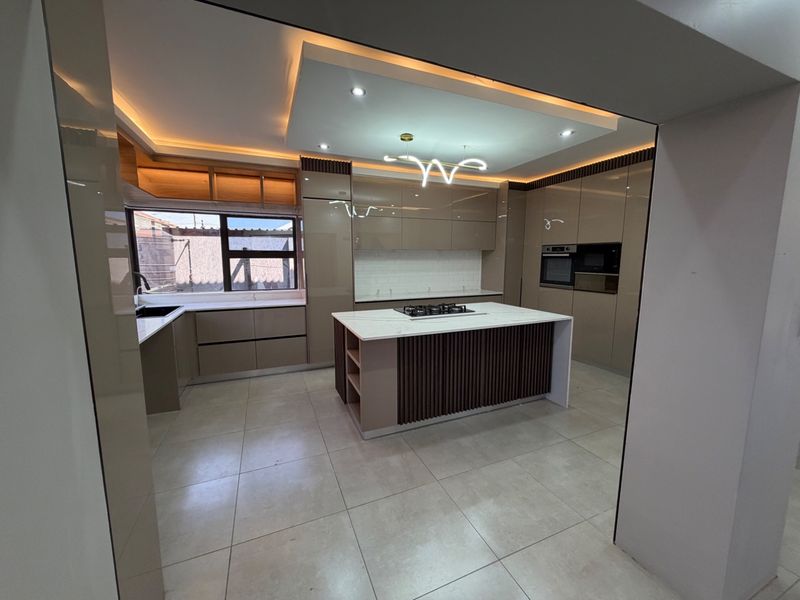 Modern, high-end kitchen featuring a central island with a gas cooktop, sleek integrated cabinetry, built-in appliances, and sophisticated recessed lighting.