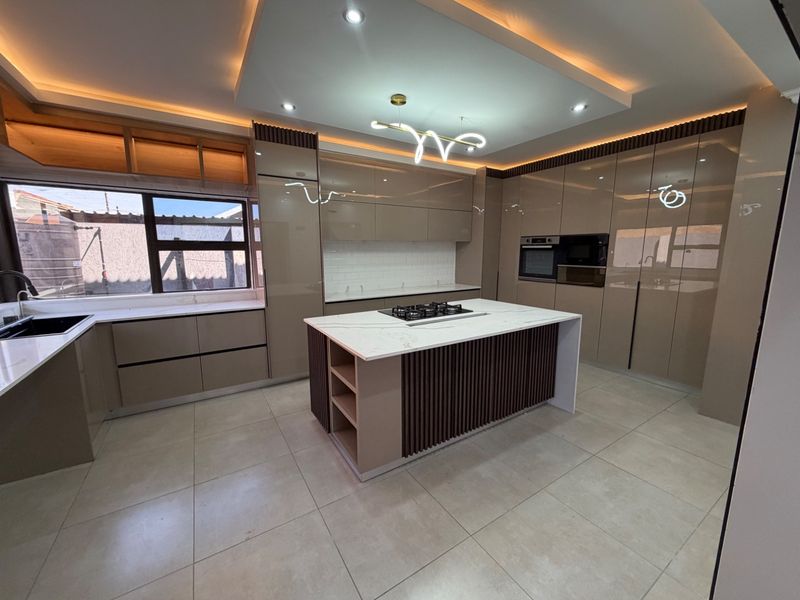 Modern, high-end kitchen featuring a central island with a gas hob, sleek cabinetry, stone countertops, and integrated appliances with sophisticated recessed lighting.