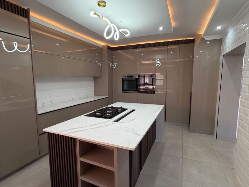 Modern kitchen featuring a central island with a gas cooktop, high-gloss cabinetry, stone countertops, and sophisticated recessed ceiling lighting.