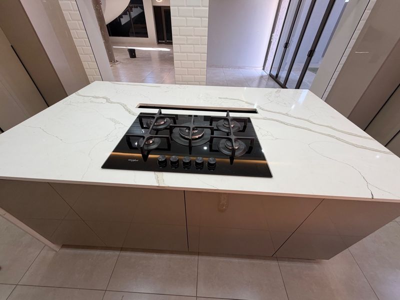 Modern kitchen island featuring a sleek stone countertop and integrated gas cooktop, set within a contemporary open-plan space with neutral finishes.