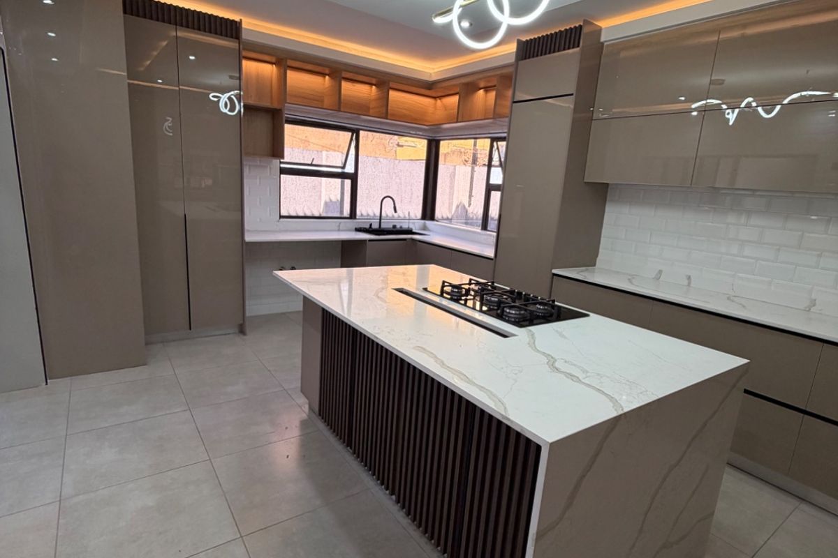 Modern kitchen featuring a central island with a gas hob, sleek high-gloss cabinetry, stone countertops, and sophisticated recessed and cove lighting.