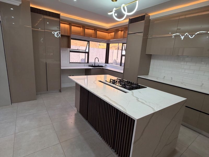 Modern kitchen featuring a central island with a gas hob, sleek high-gloss cabinetry, stone countertops, and sophisticated recessed and cove lighting.