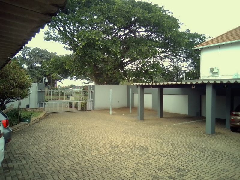 A paved communal parking area featuring covered carport bays, secure perimeter walling, and an automated entrance gate.