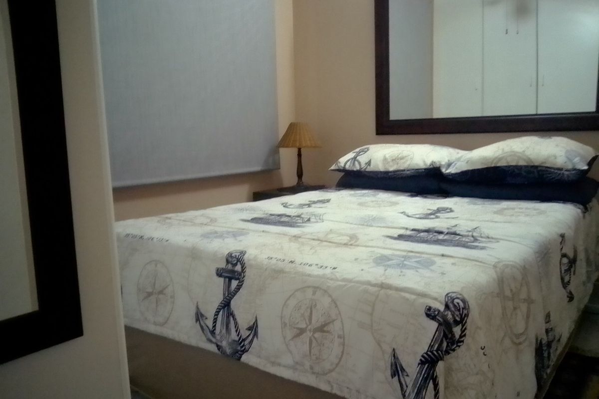 A bedroom featuring built-in cupboards, a ceiling fan, and a roller blind, providing a functional sleeping space.