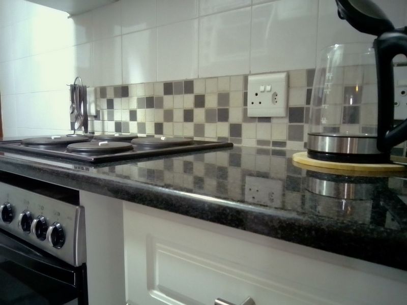 A functional kitchen area featuring a dark granite countertop, built-in electric hob, oven, and a decorative tiled backsplash.