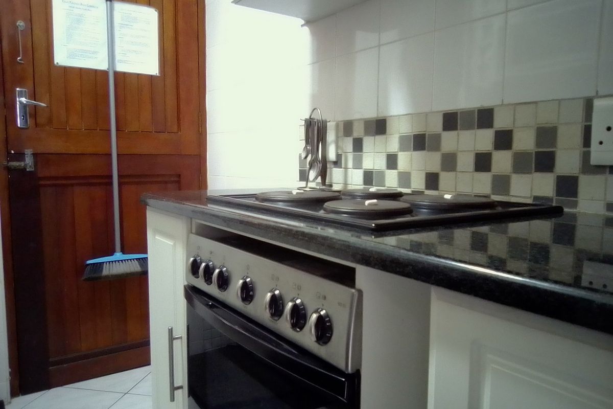 A functional kitchen area featuring a built-in oven, electric hob, extractor fan, granite countertops, and tiled backsplash with fitted cabinetry.
