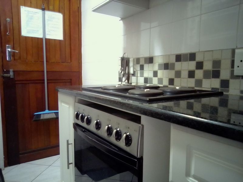A functional kitchen area featuring a built-in oven, electric hob, extractor fan, granite countertops, and tiled backsplash with fitted cabinetry.