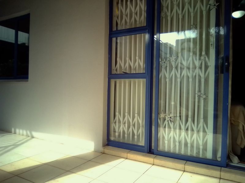 A covered patio area featuring tiled flooring, a sliding glass door with a security gate, and a window looking into the interior.