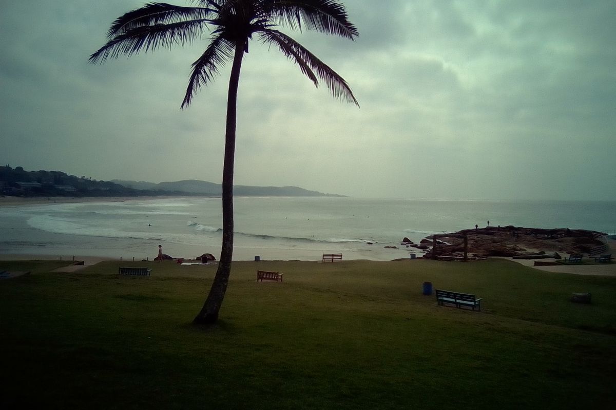 A scenic coastal view overlooking the beach, rocky shoreline, and ocean horizon under an overcast sky.