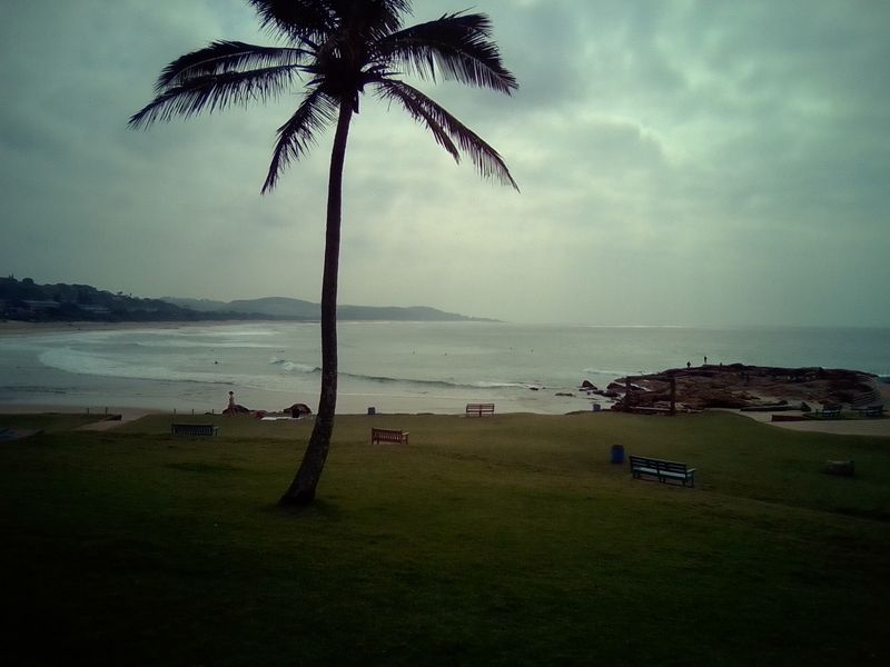 A scenic coastal view overlooking the beach, rocky shoreline, and ocean horizon under an overcast sky.