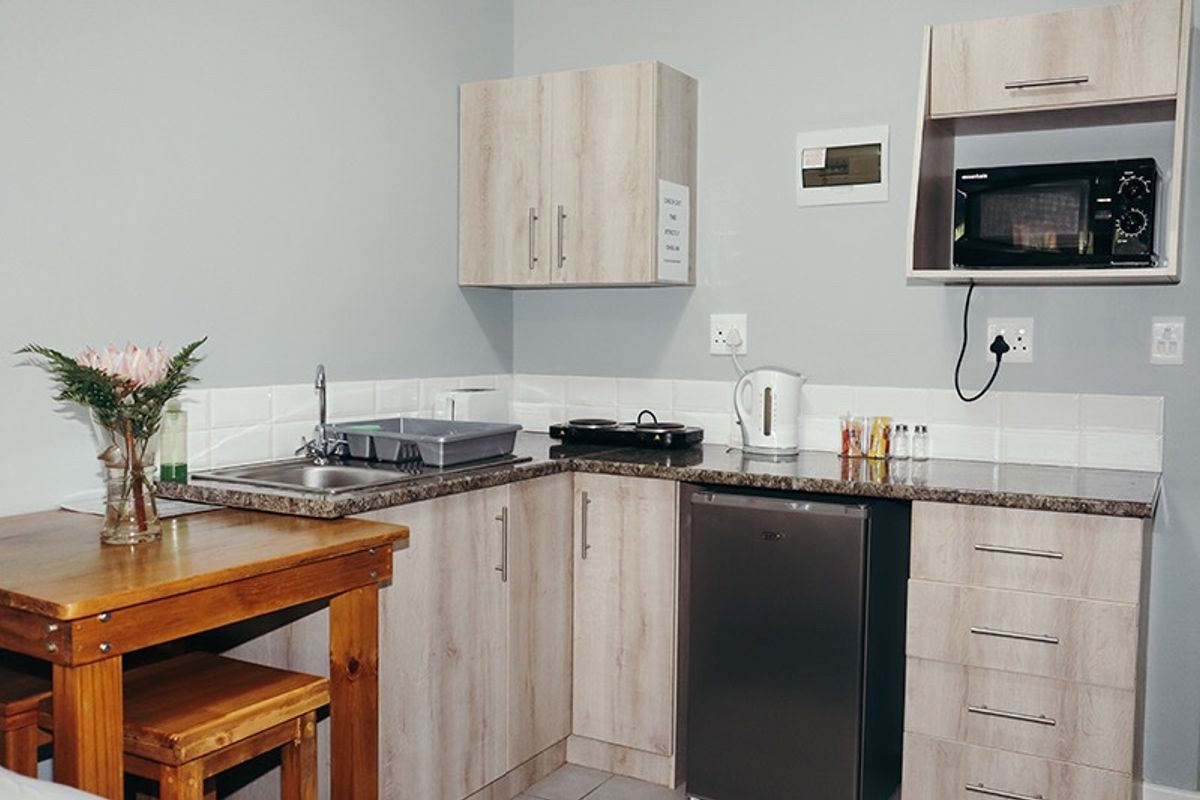 Compact kitchenette featuring light wood-grain cabinetry, granite countertops, tiled backsplash, and integrated microwave storage, suitable for a small farm cottage or studio unit.