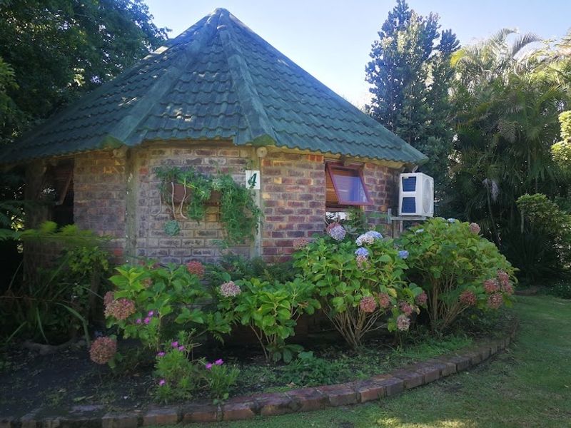 A charming circular brick cottage with a tiled roof, surrounded by lush garden landscaping and mature greenery.