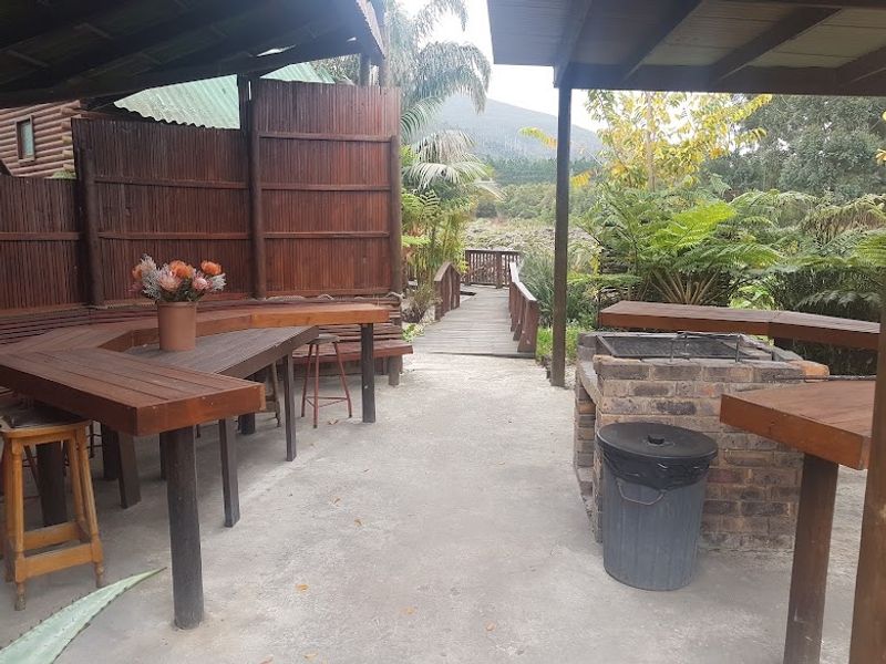 Covered outdoor entertainment area featuring a built-in brick braai, timber decking, and privacy screening, overlooking a garden walkway.