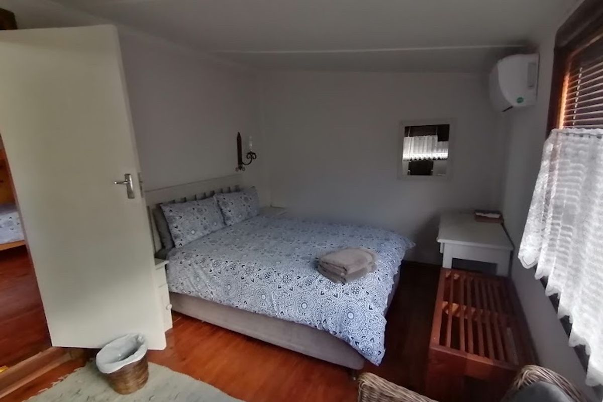 A cozy bedroom featuring hardwood flooring, a wall-mounted air conditioning unit, and window blinds.