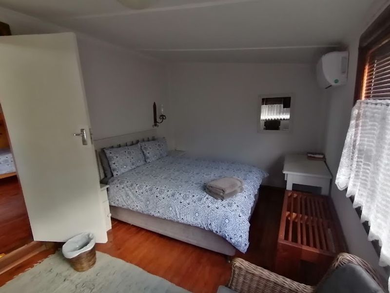 A cozy bedroom featuring hardwood flooring, a wall-mounted air conditioning unit, and window blinds.