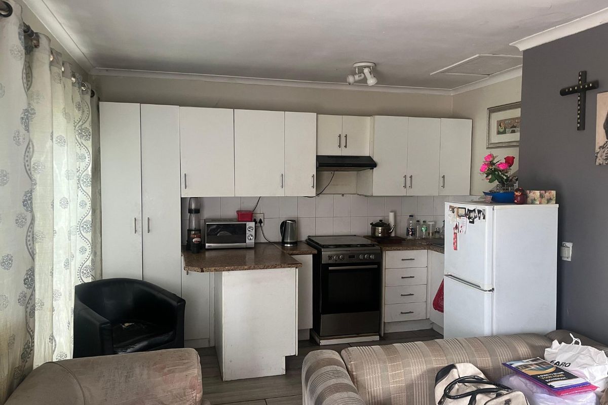 Compact kitchen featuring white built-in cabinetry, laminate countertops, a tiled backsplash, and a freestanding stove with an extractor fan.