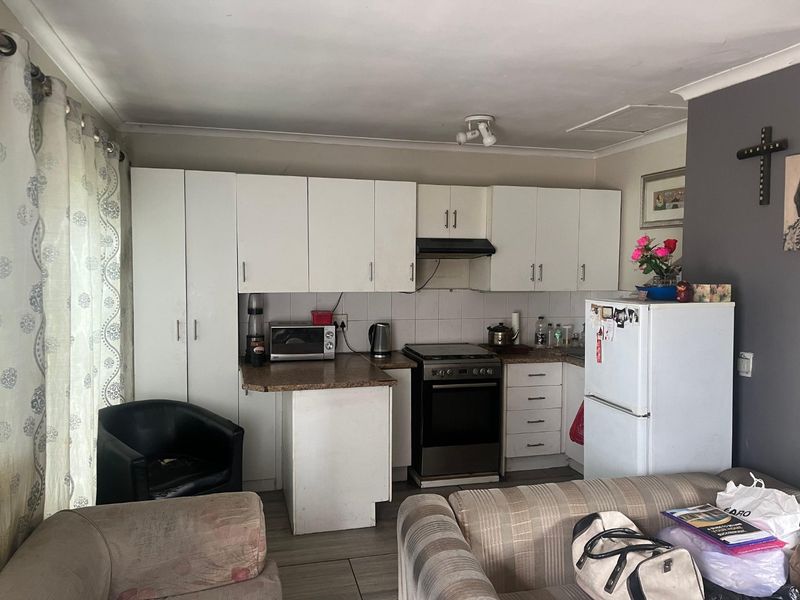 Compact kitchen featuring white built-in cabinetry, laminate countertops, a tiled backsplash, and a freestanding stove with an extractor fan.