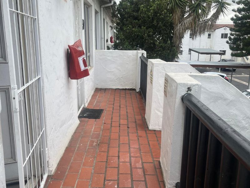 An exterior balcony featuring terracotta tile flooring, a metal balustrade, and a security gate entrance.