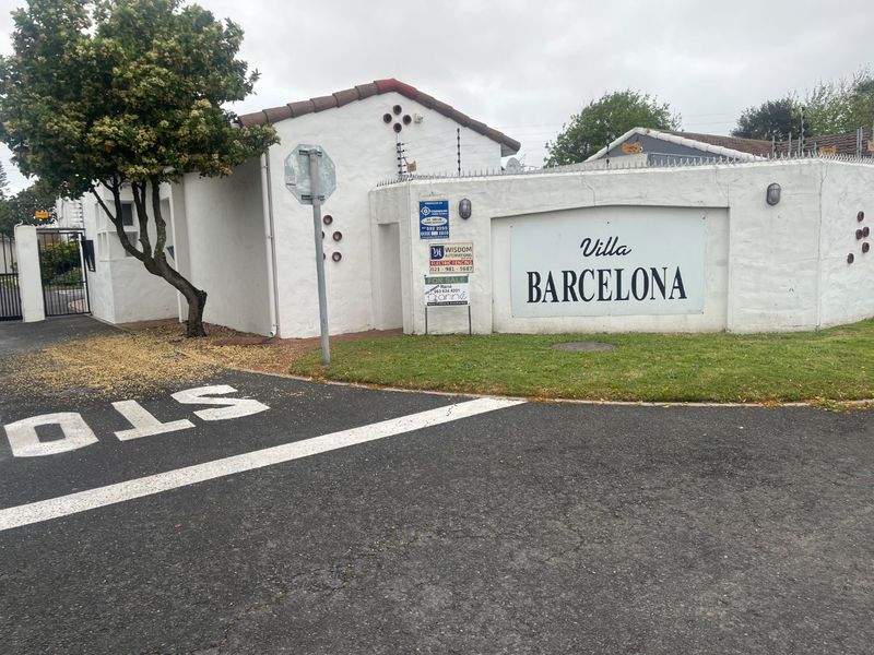 Front entrance view of Villa Barcelona apartment complex featuring a boundary wall with electric fencing and security gate access.