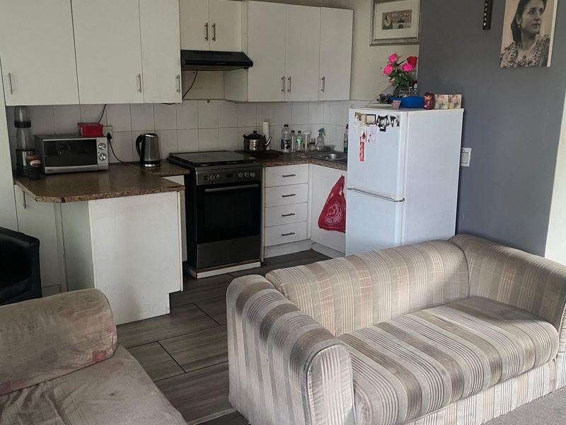 Open-plan kitchen and living area featuring white cabinetry, laminate countertops, and tiled flooring, offering a functional layout for modern apartment living.