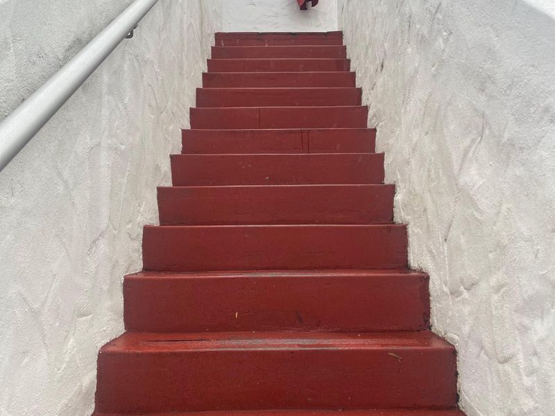 Exterior staircase with red painted steps and white textured walls leading to an apartment entrance.