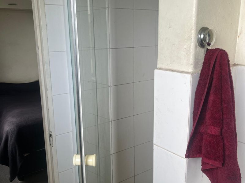 A compact bathroom featuring a glass shower enclosure with white wall tiles and a tiled floor, showing signs of wear.