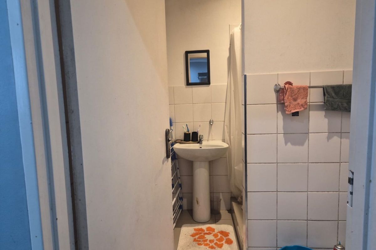 A compact bathroom featuring a pedestal basin, tiled walls, and a shower area, requiring cosmetic updates to improve its overall condition.