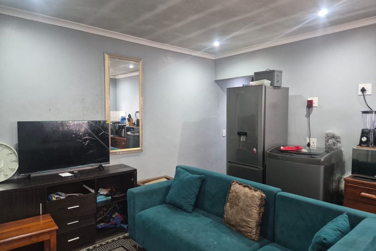 A living room area featuring recessed downlighting and coved ceilings, with visible wall wear requiring minor maintenance.