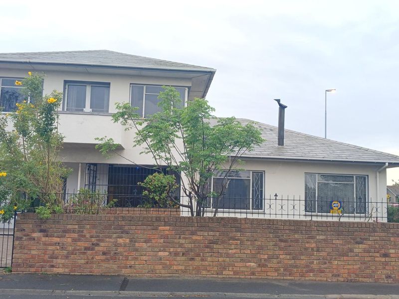 Front view of a two-story residential house featuring a brick boundary wall, security gates, and a tiled roof structure.
