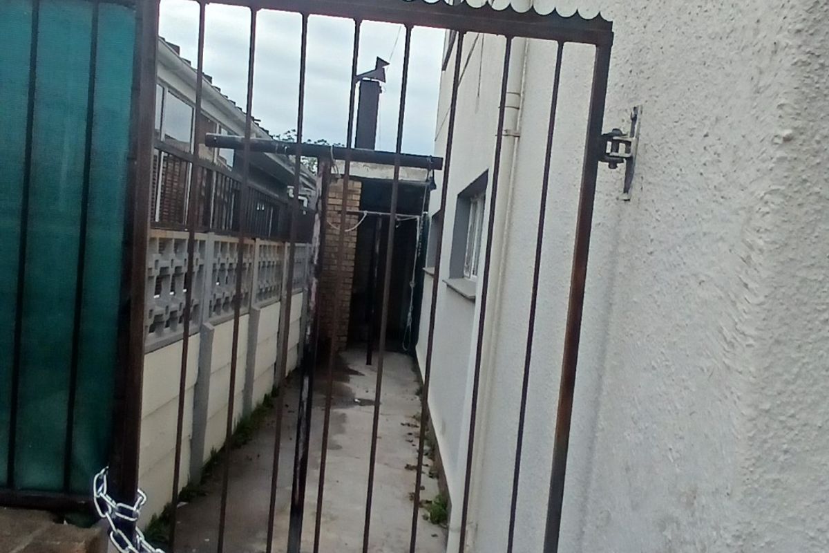 A narrow side passage featuring a metal security gate, concrete pathway, and exterior wall with a mounted satellite dish.