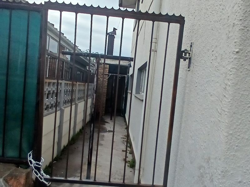 A narrow side passage featuring a metal security gate, concrete pathway, and exterior wall with a mounted satellite dish.