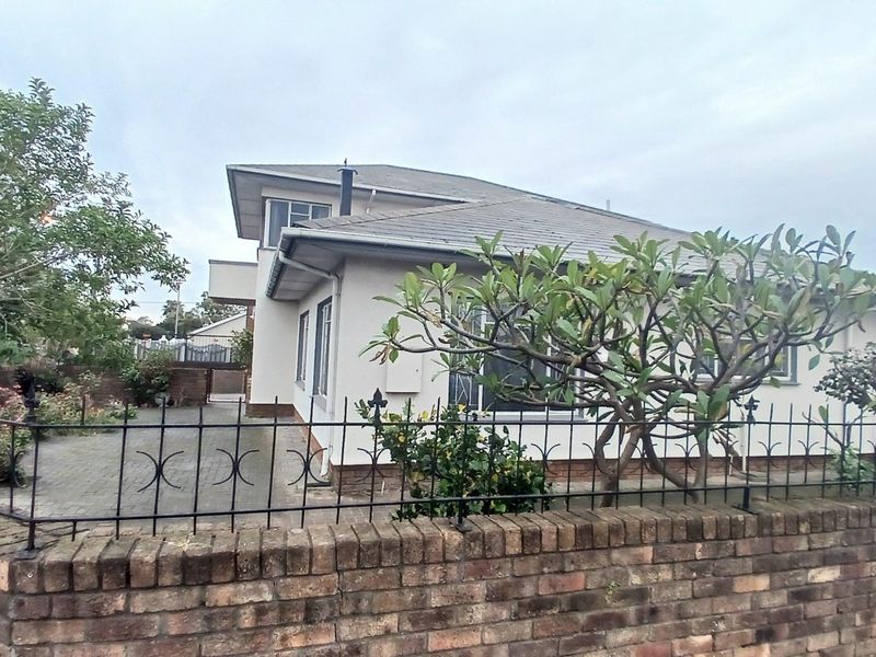 Front view of a residential property featuring a brick boundary wall, wrought iron fencing, and a paved driveway leading to the house.