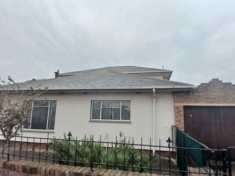 Front exterior view of a single-story house featuring a tiled roof, brick boundary wall with metal fencing, and an integrated garage.