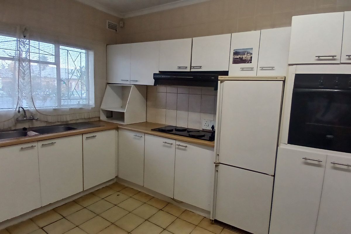 Functional kitchen featuring white built-in cabinetry, electric hob, integrated oven, double sink, and tiled flooring with a window providing natural light.