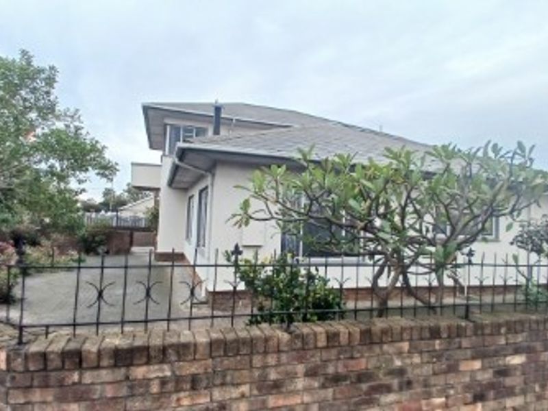 Front view of a residential property featuring a brick boundary wall, wrought iron fencing, a paved driveway, and a tiled roof structure.