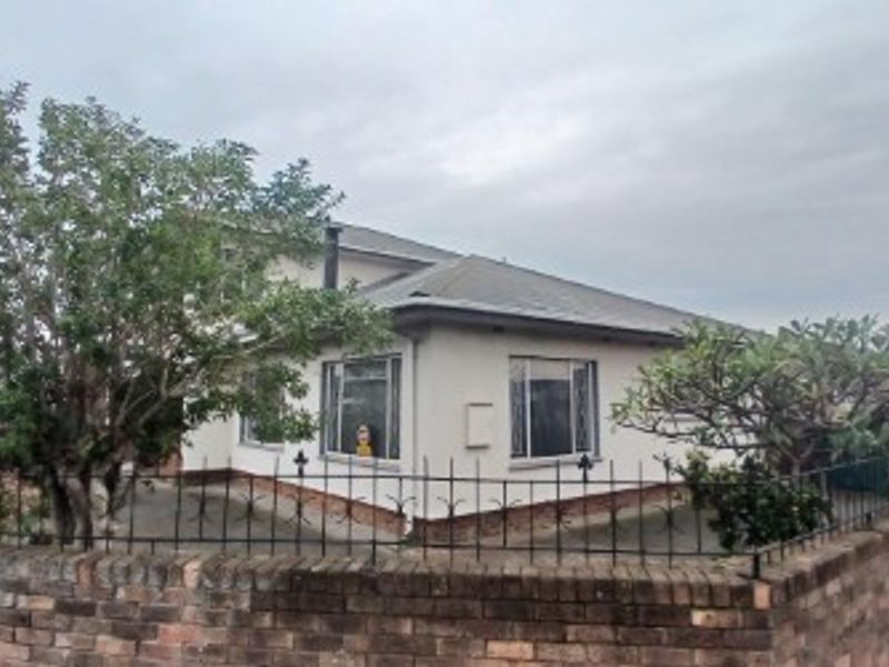 A street-facing view of a single-story house featuring a brick boundary wall, wrought iron fencing, and a metal roof.