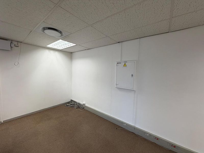 A clean, empty office space featuring a suspended ceiling, recessed lighting, carpeted flooring, and integrated electrical distribution and trunking systems.
