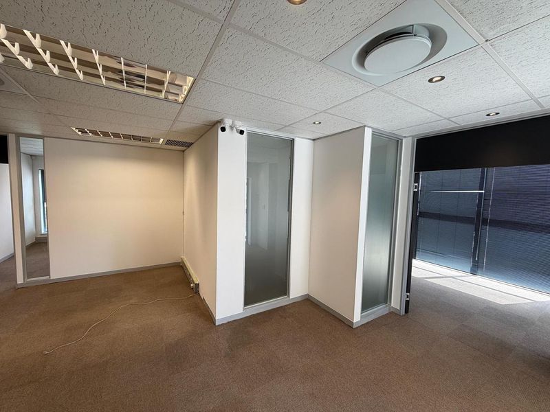 A vacant, well-lit office space featuring suspended ceilings, glass partitions, carpeted flooring, and integrated air conditioning, suitable for a professional workspace.