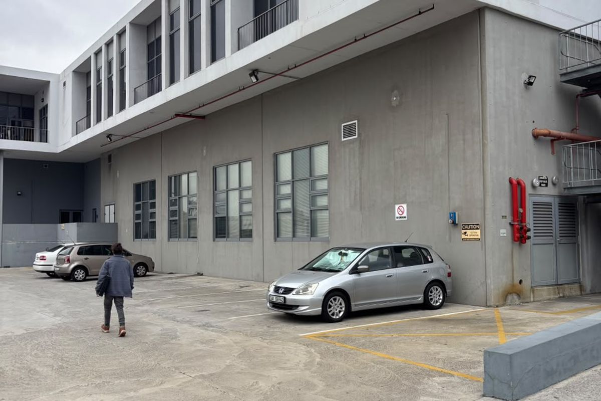 Rear exterior view of a modern industrial building featuring concrete facade, large windows, and dedicated parking area with visible fire safety infrastructure.