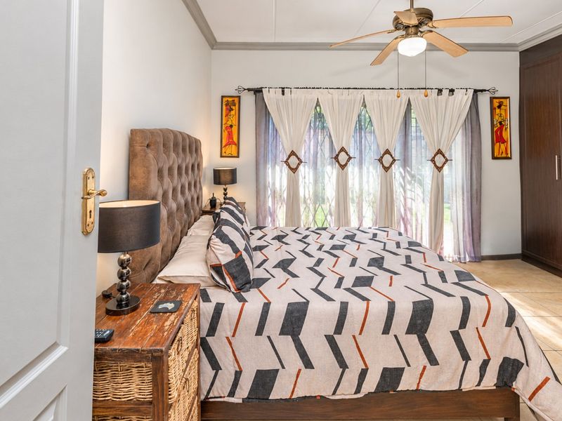A well-maintained bedroom featuring tiled flooring, a ceiling fan, and built-in cupboards with direct access to the garden through a sliding door.