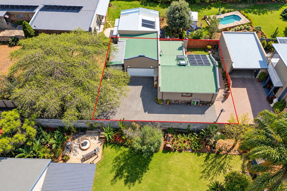 Aerial view of the property highlighting the main dwelling with a green metal roof, solar installations, paved driveway, and surrounding garden area.