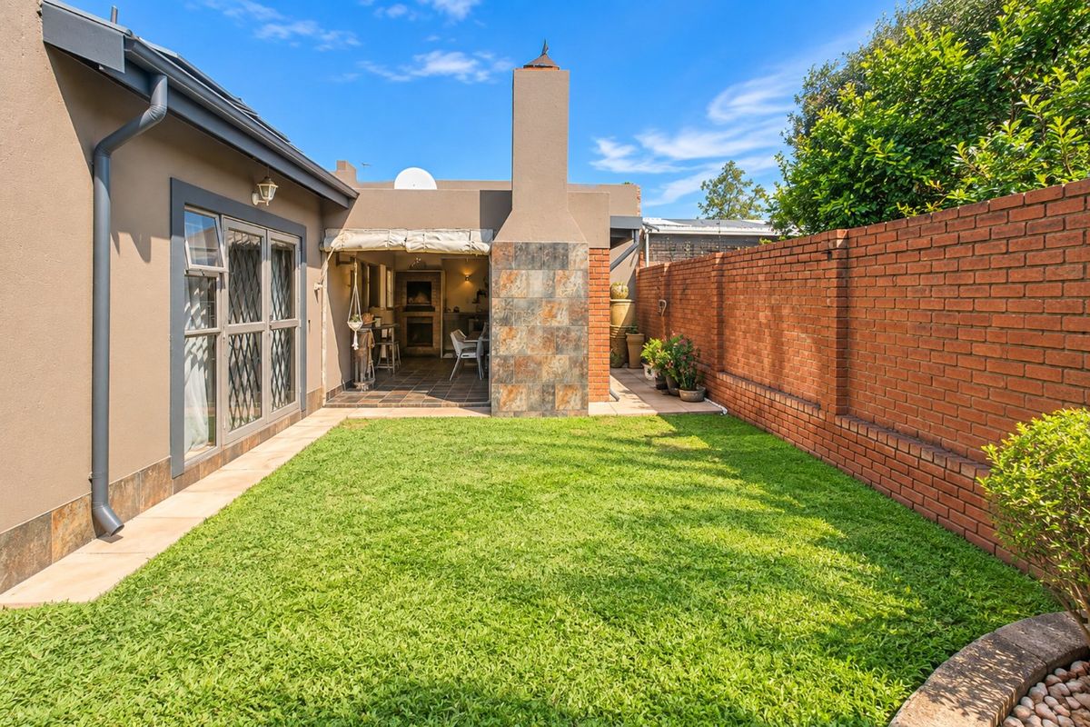 A well-maintained rear garden featuring a brick boundary wall, a paved patio area with a built-in fireplace, and a neat lawn.