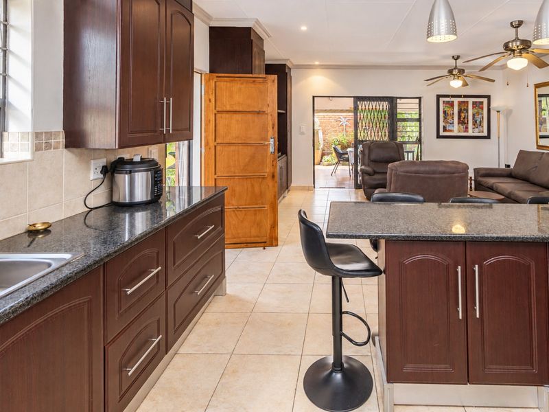 Open-plan kitchen and living area featuring dark wood cabinetry, granite countertops, tiled flooring, and direct access to an outdoor patio space.