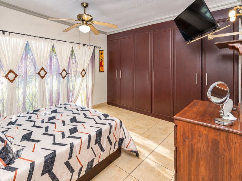 A well-maintained bedroom featuring extensive built-in dark wood cabinetry, tiled flooring, and a ceiling fan, offering ample storage space.
