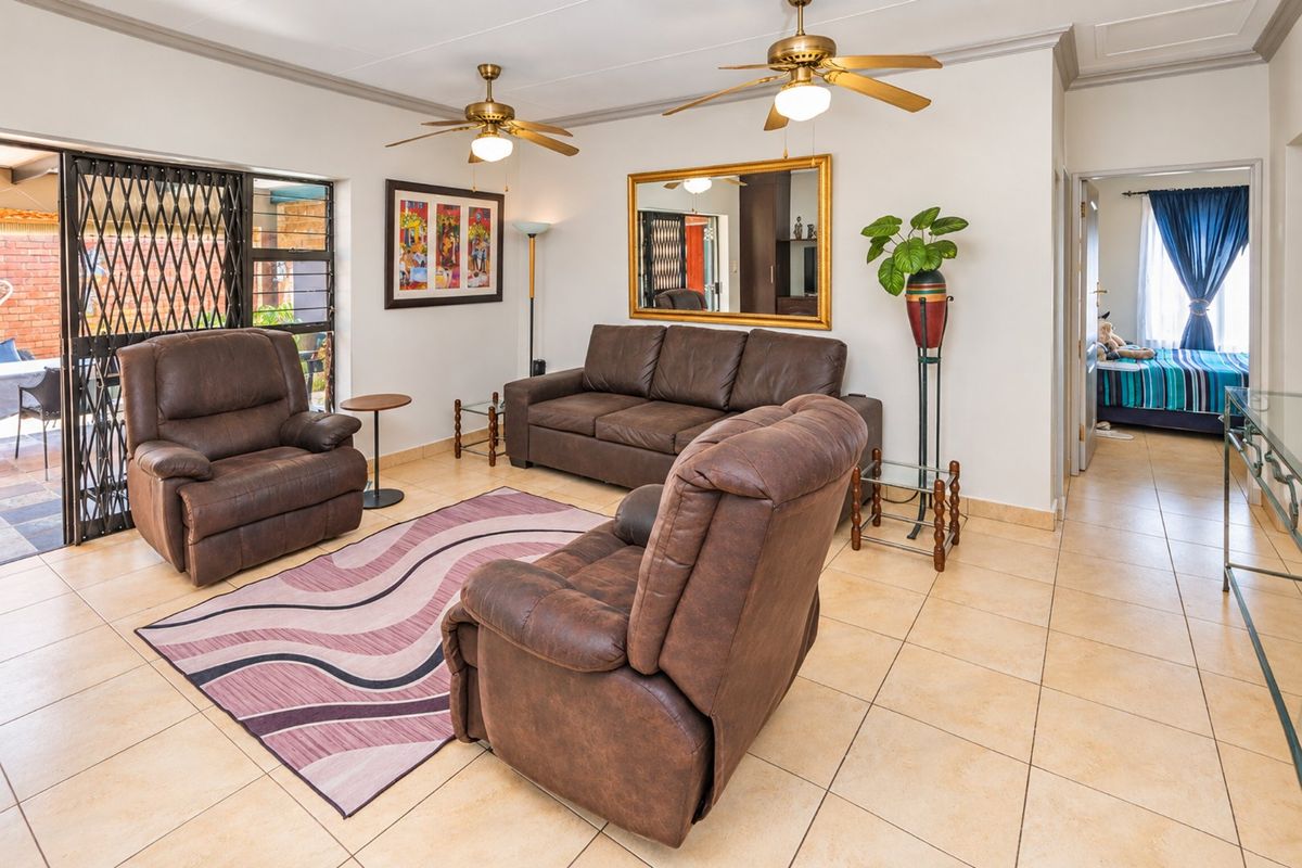 A spacious living room featuring tiled flooring, dual ceiling fans, and a sliding glass door providing access to the outdoor patio area.