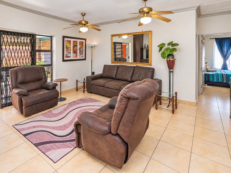 A spacious living room featuring tiled flooring, dual ceiling fans, and a sliding glass door providing access to the outdoor patio area.